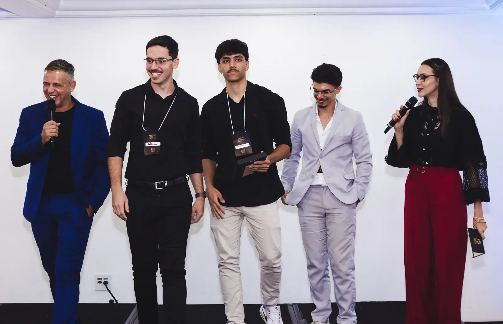 Os três sócios da CC Corps no palco, ao lado dos apresentadores, ao receber o Prêmio Excelência em Entrega 2025 em São Paulo